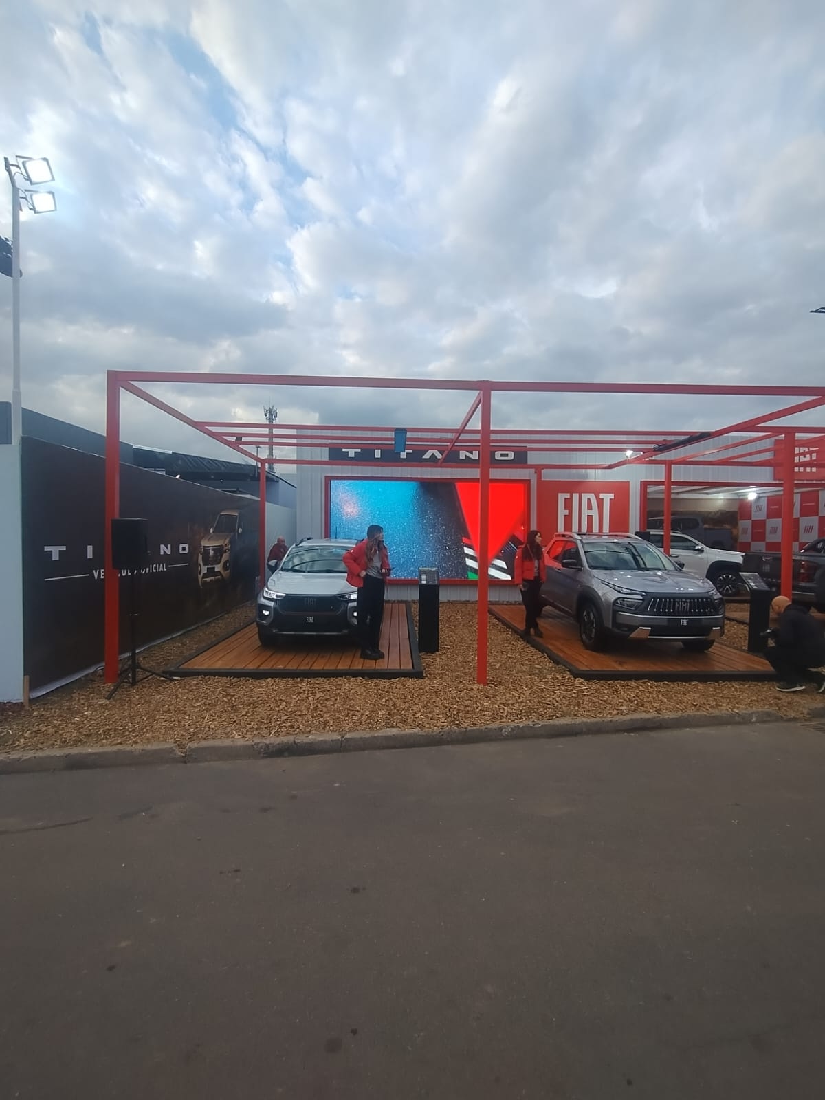Pantalla LED encendida y un altavoz dentro de un stand exterior de exhibición de vehículos.